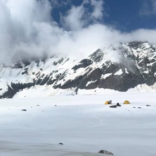 Two small tents on a snowy plateau below cloud-covered mountains