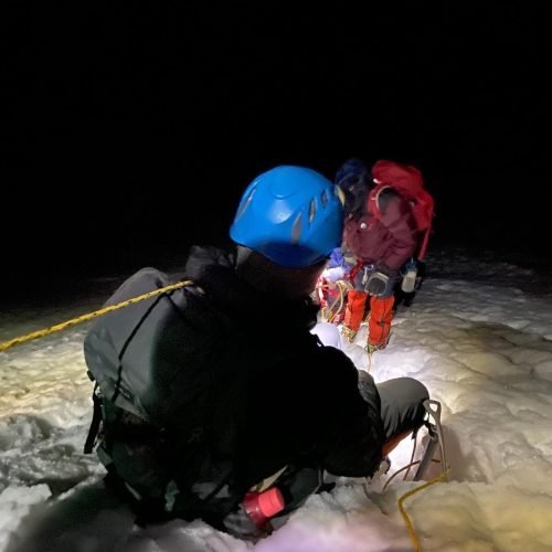 Roped climbers preparing on snow by headlamp at night